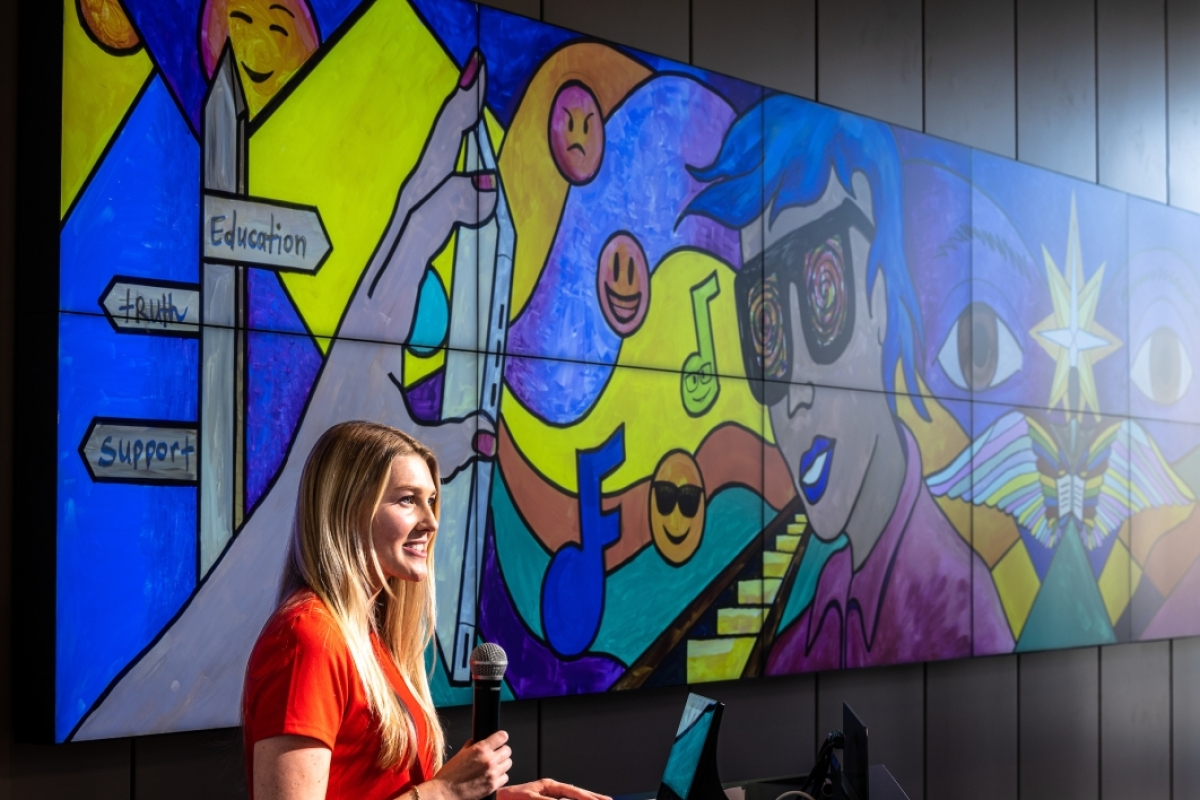 Woman speaking in front of large, colorful digital mural