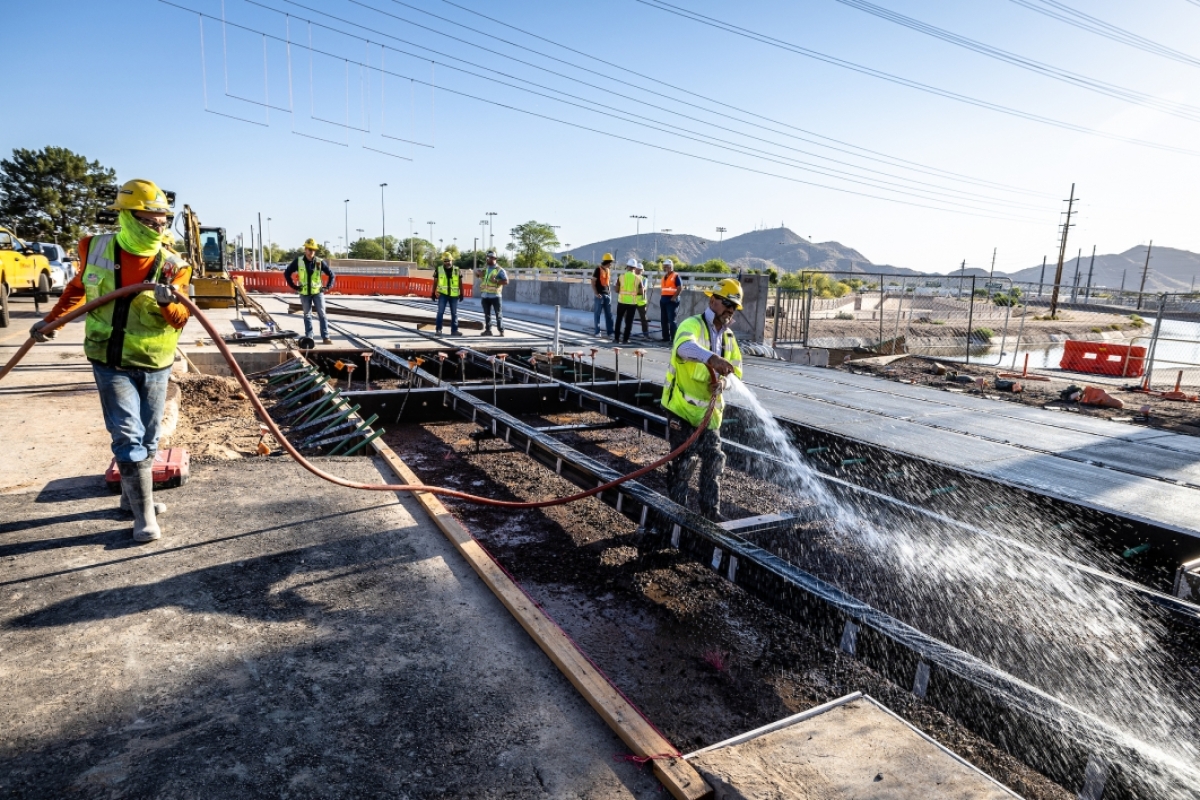 Construction workers spray water and pour a section of concrete for a light rail extension