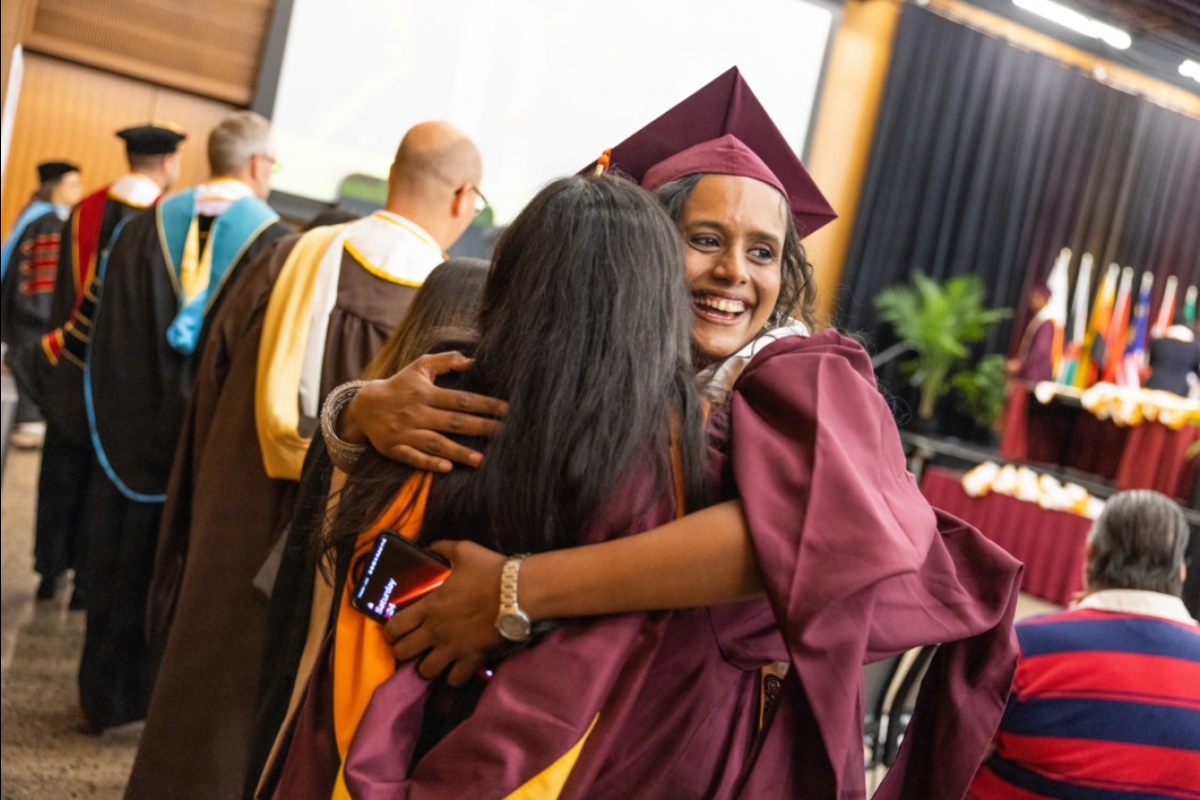 Two graduates hug at commencement ceremony