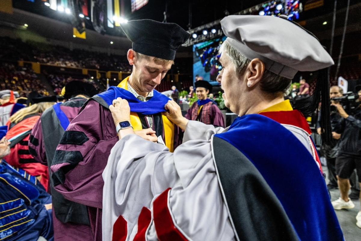 Faculty advisor helping graduate with his hood at commencement
