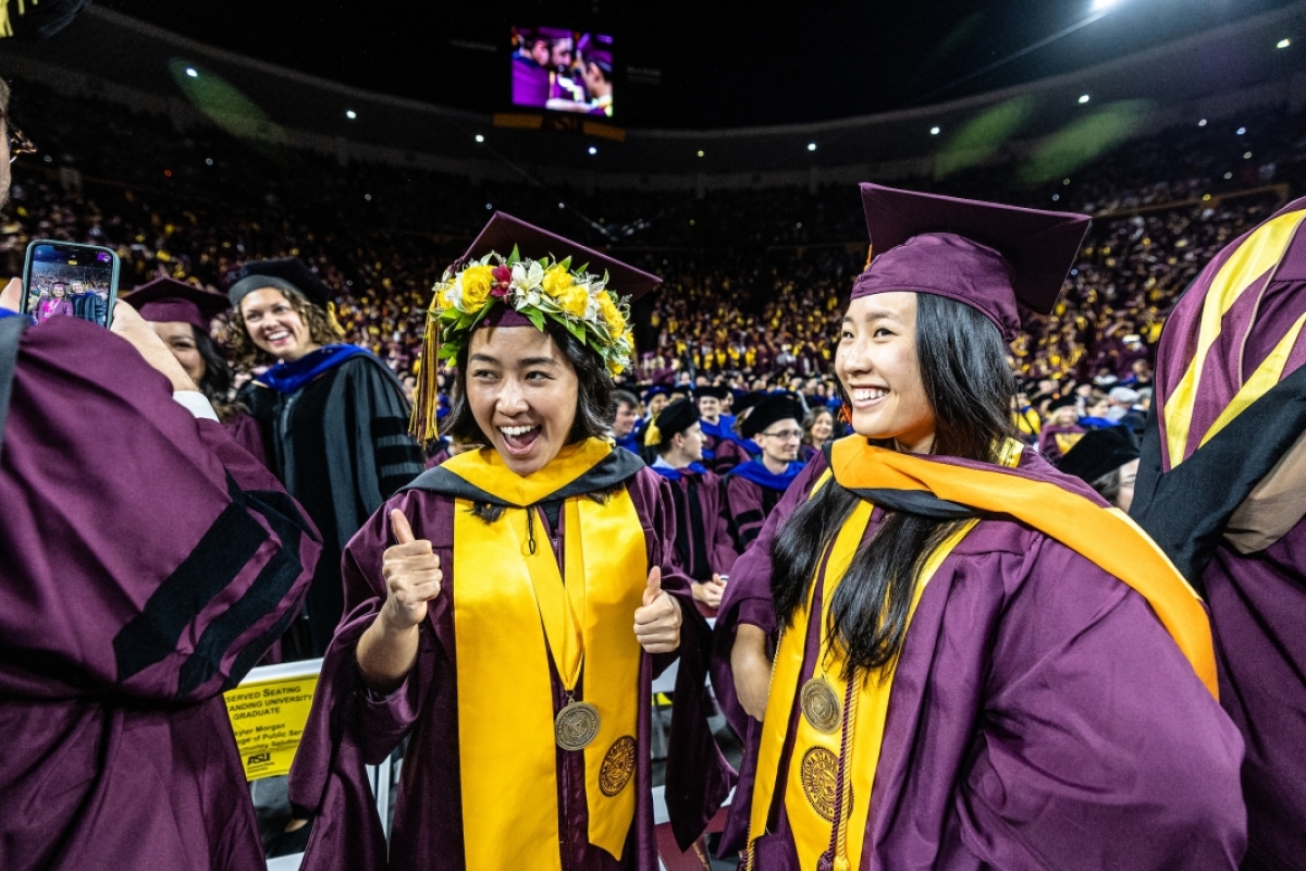 Two graduates in maroon caps and gowns smiling during convocation