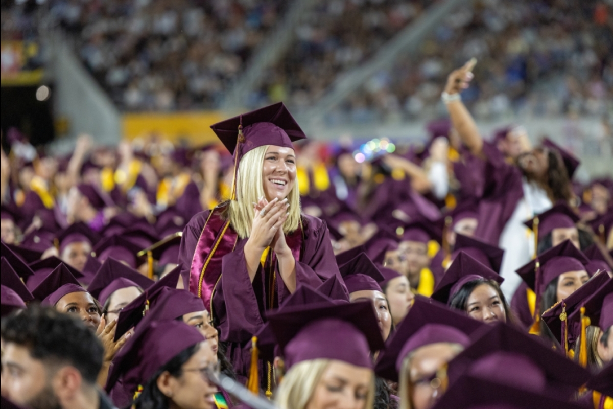 Woman standing up in crowd of graduates during commencement
