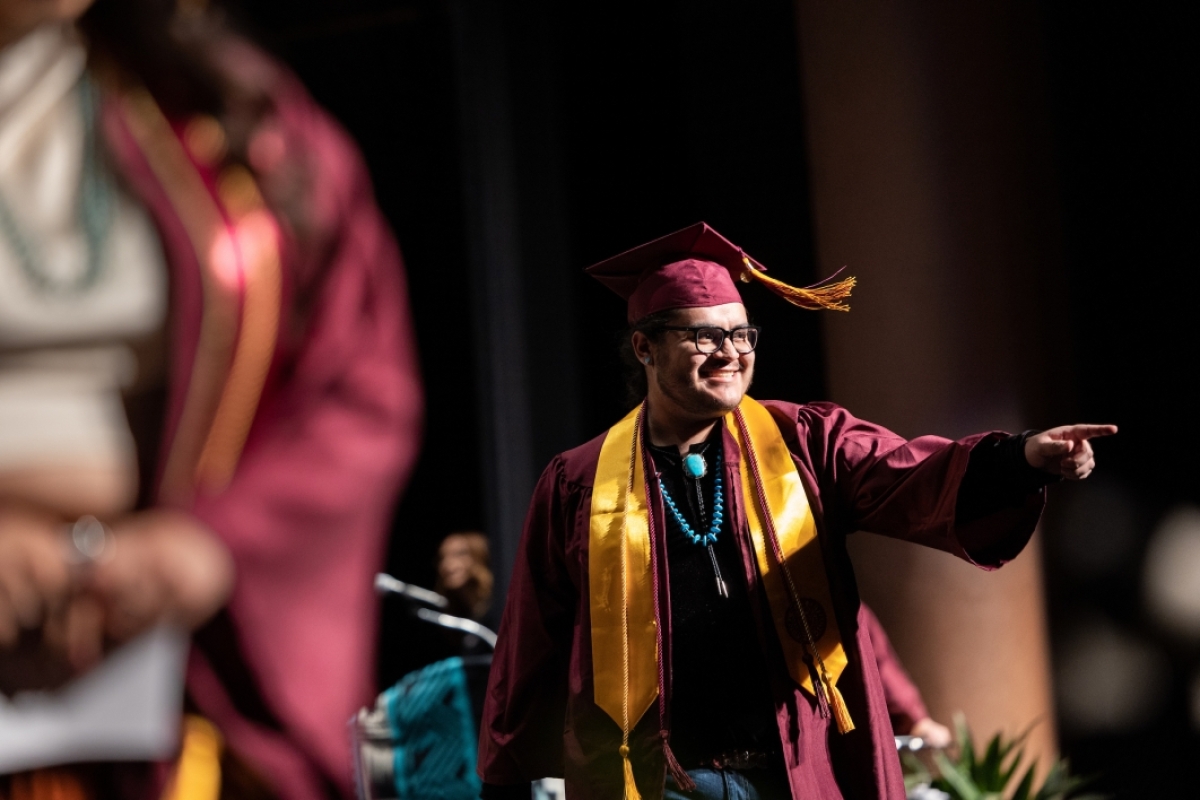 Graduate pointing to audience as he crosses stage at convocation