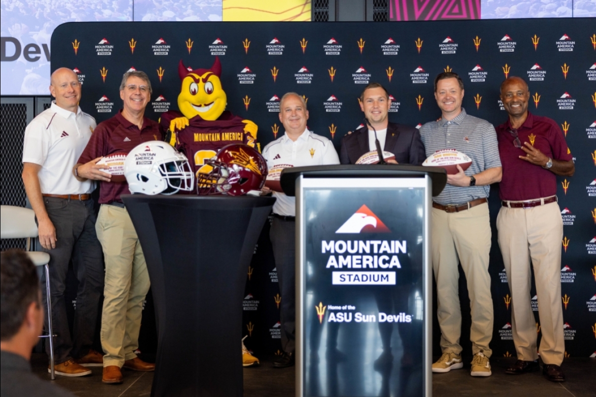 A line of people pose with footballs and the ASU Sparky mascot