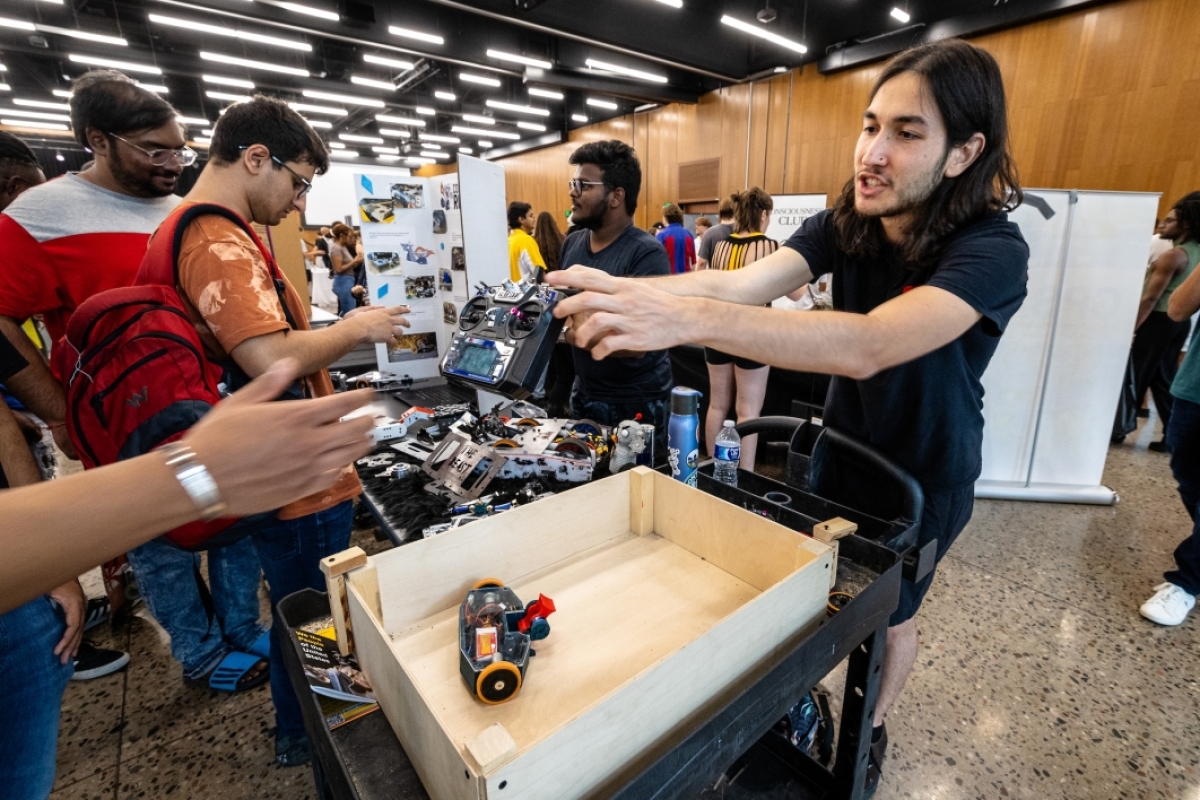 Student hands another student a robot controller during club showcase