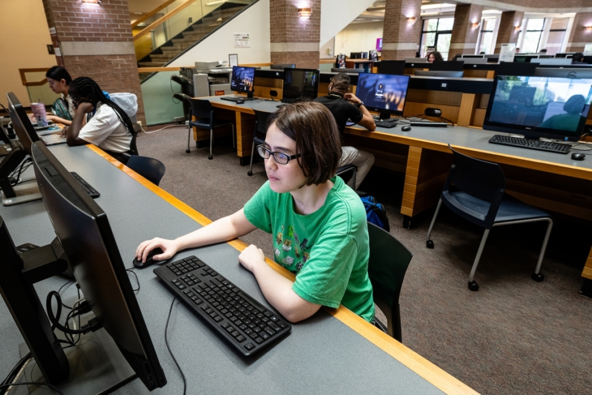 Student wearing green shirt and glasses working on computer in library