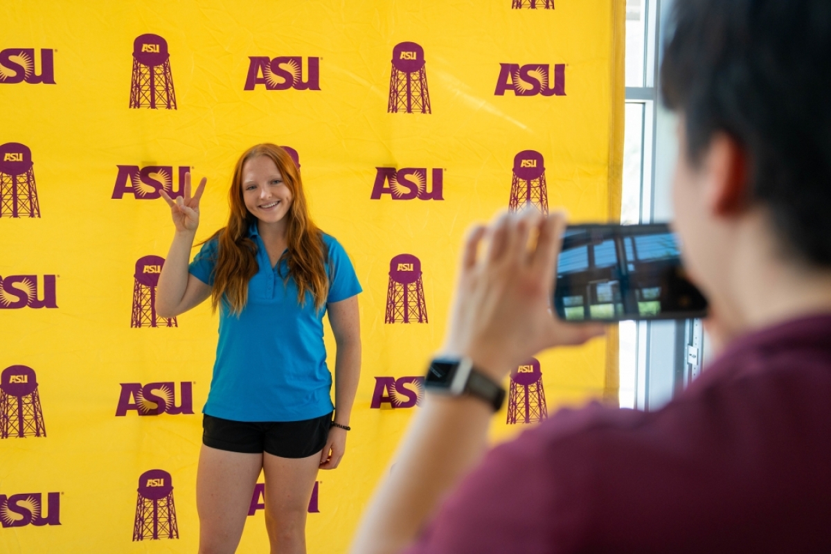 Staff member taking photo of student in front of ASU background