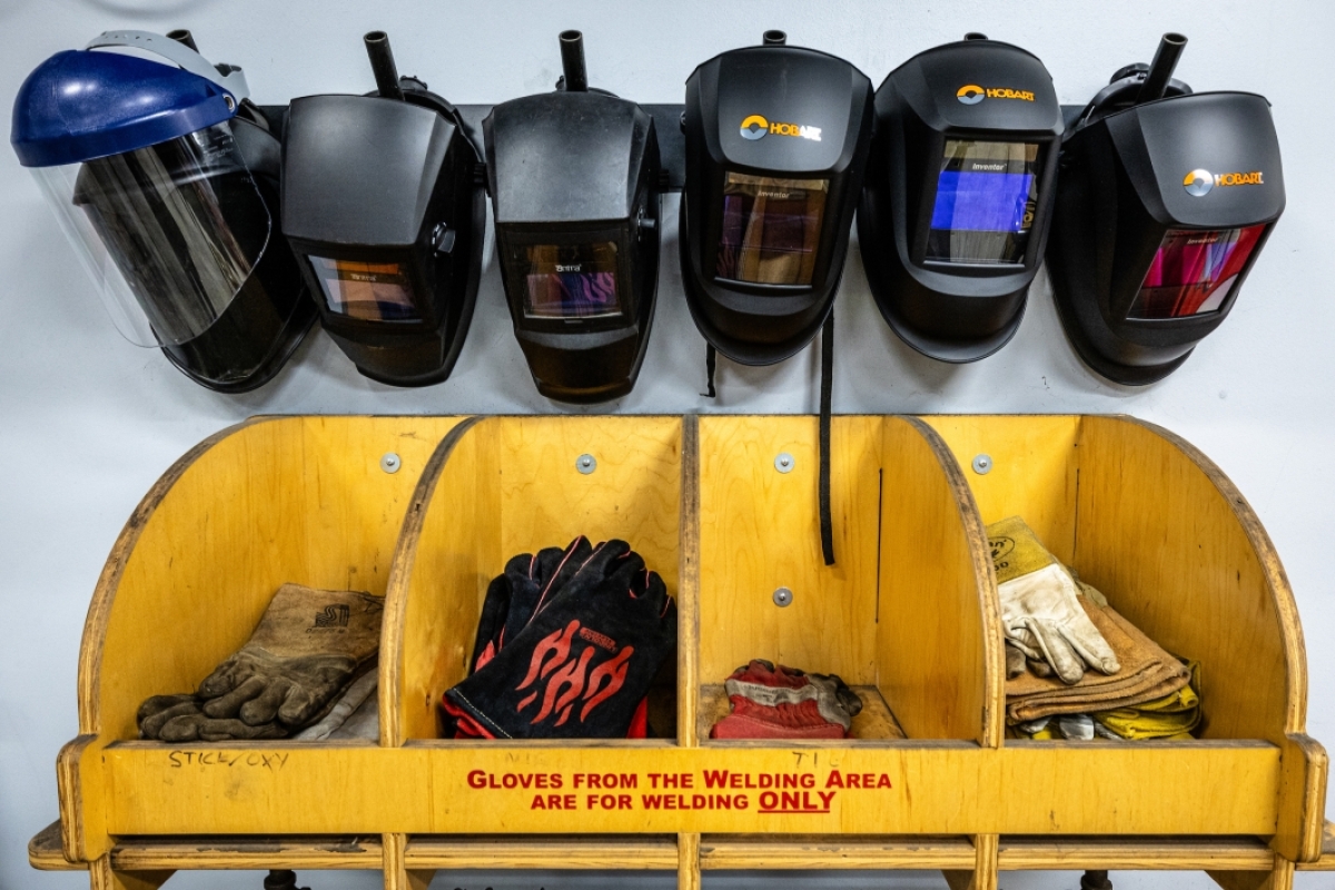 Welding helmets and gloves hanging on a wall.