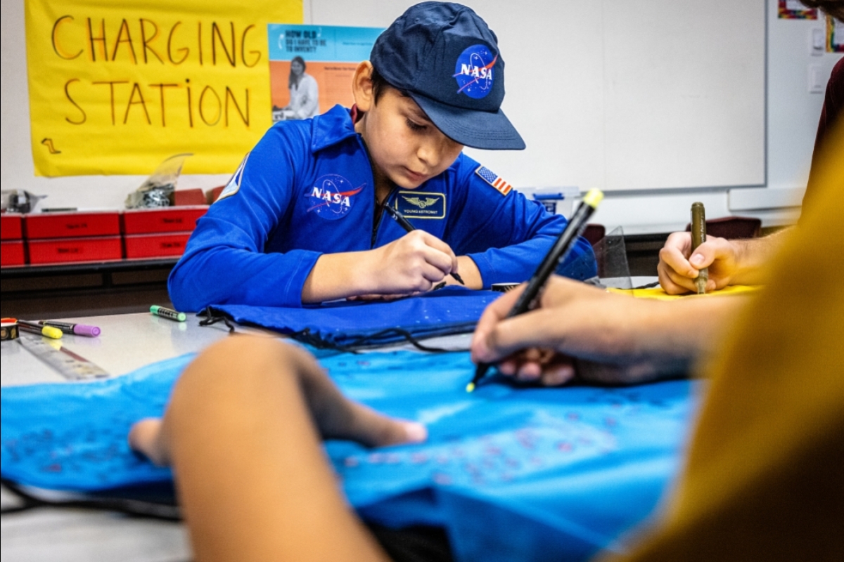 A middle school boy wearing a NASA costume draws on a bag