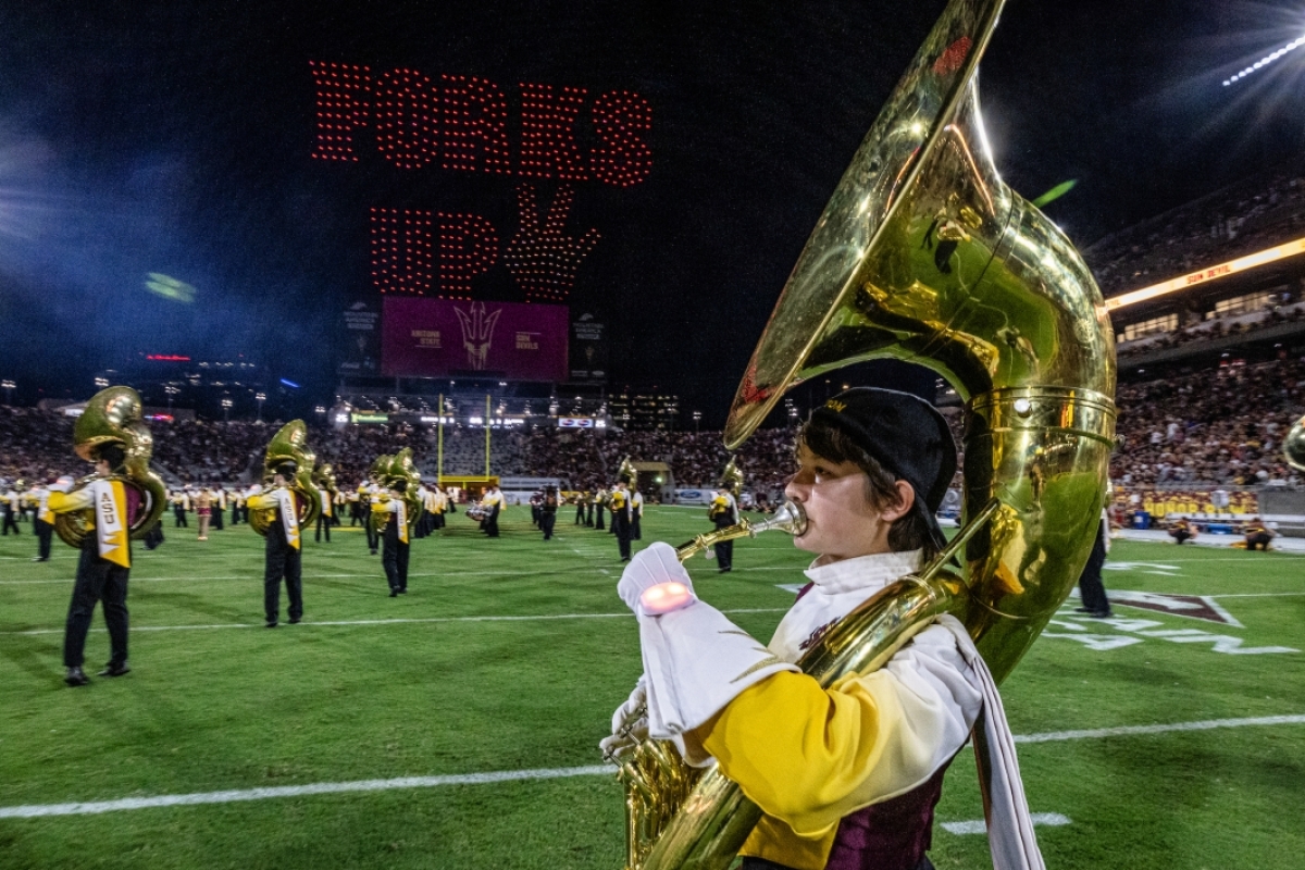 A tuba player performs with the ASU marching band while drones spell out Forks Up in the air