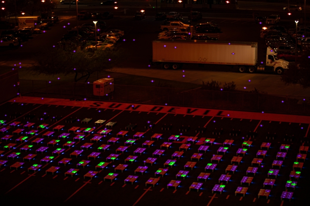 Lighted drones take off from a parking lot