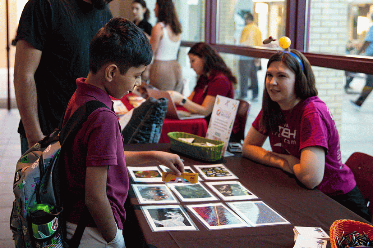 A woman speaks to an elementary student at a tabling event