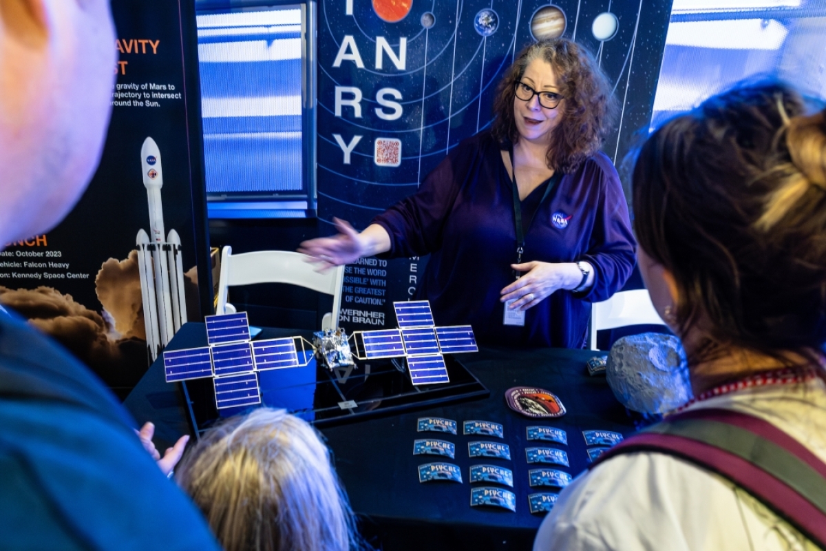 A woman speaks to visitors at a NASA tabling event