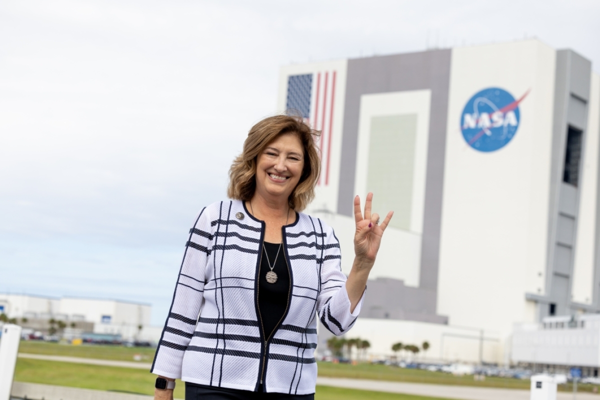A woman standing in front of a NASA building does an ASU pitchfork gesture