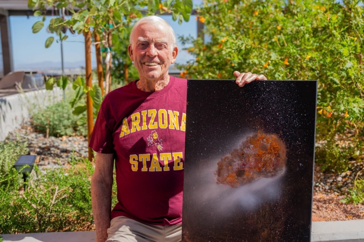 A man smiles while holding a painting of an asteroid