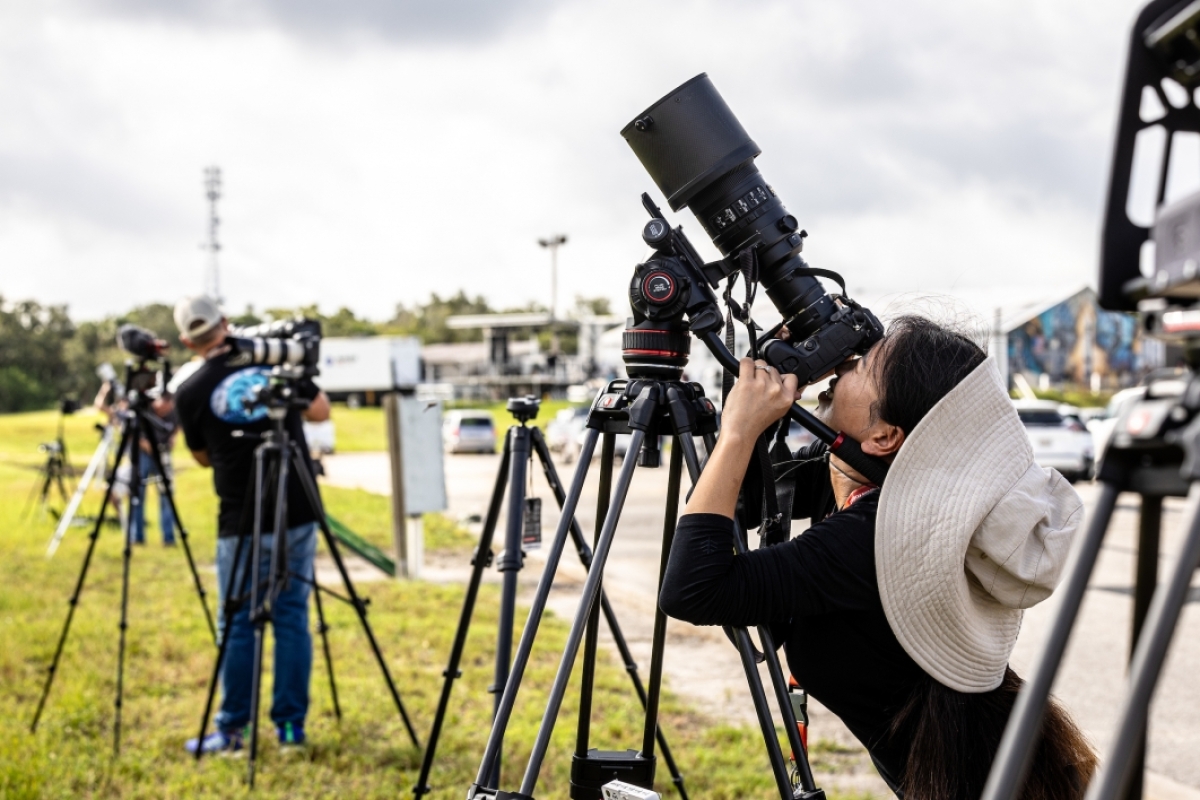 A woman looks through a camera with an enormous lens pointed at the sky