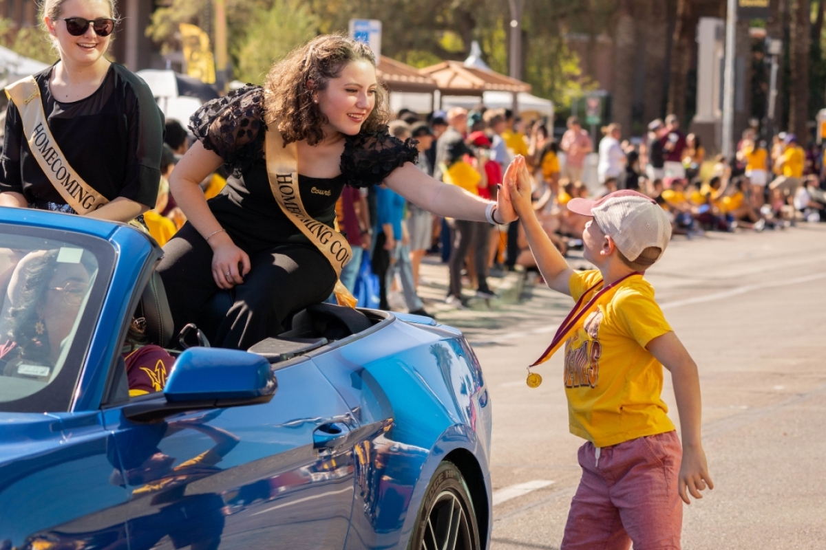 Kid high-fiving ASU Homecoming royalty in a car in a parade