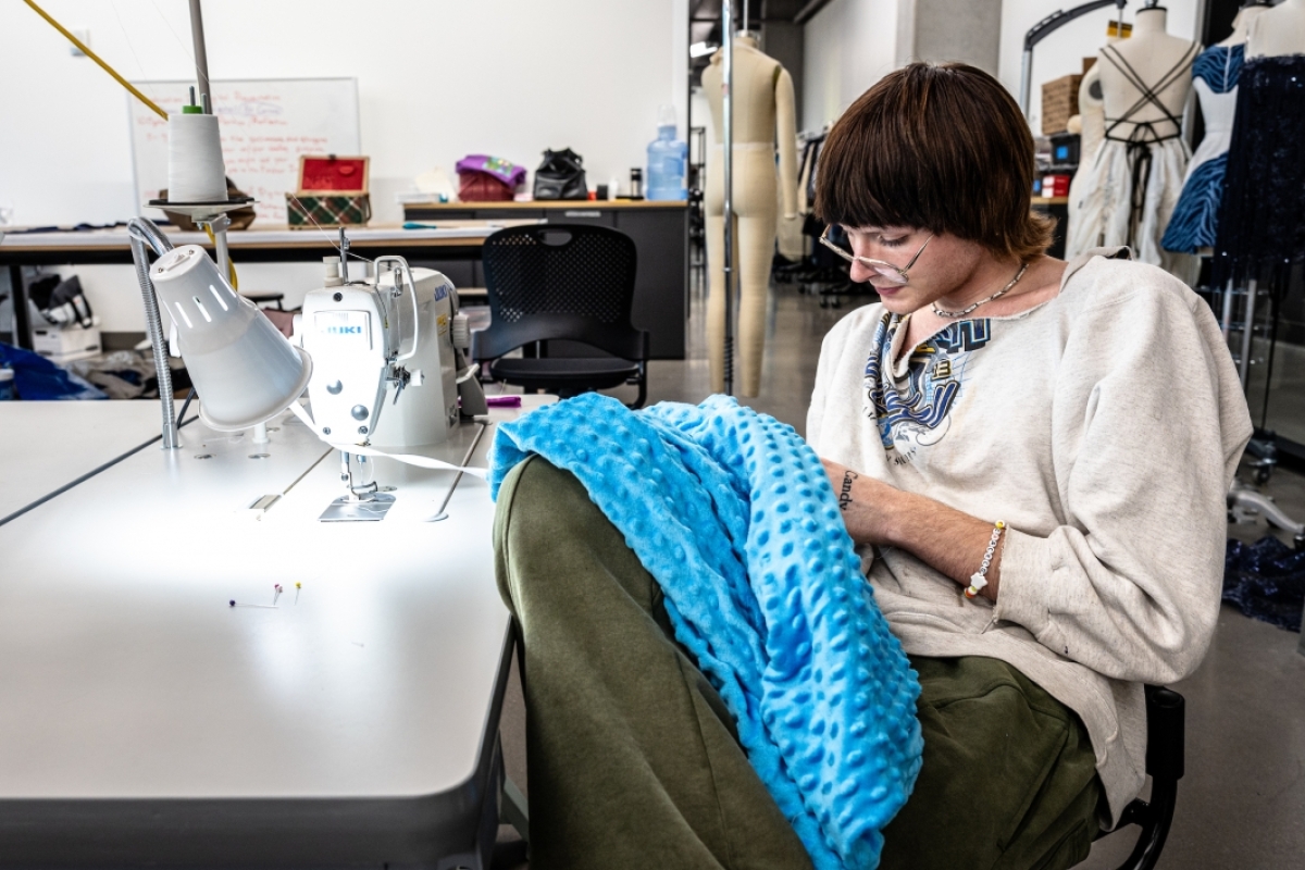 Student seated in a workspace sewing a garment.