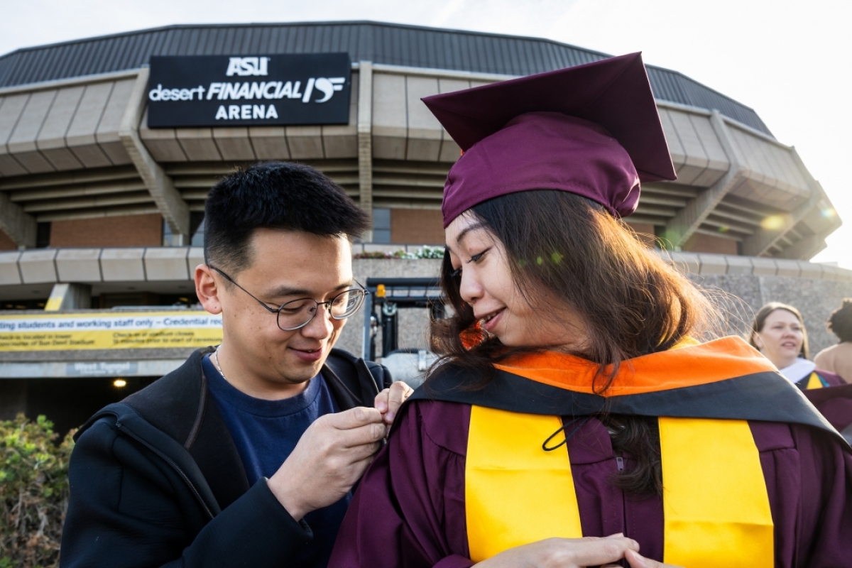Man helping pin doctoral hood on woman who is graduating