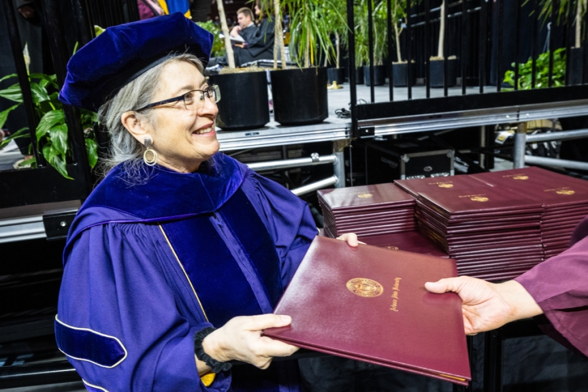 Woman in graduation regalia holding out diploma covers