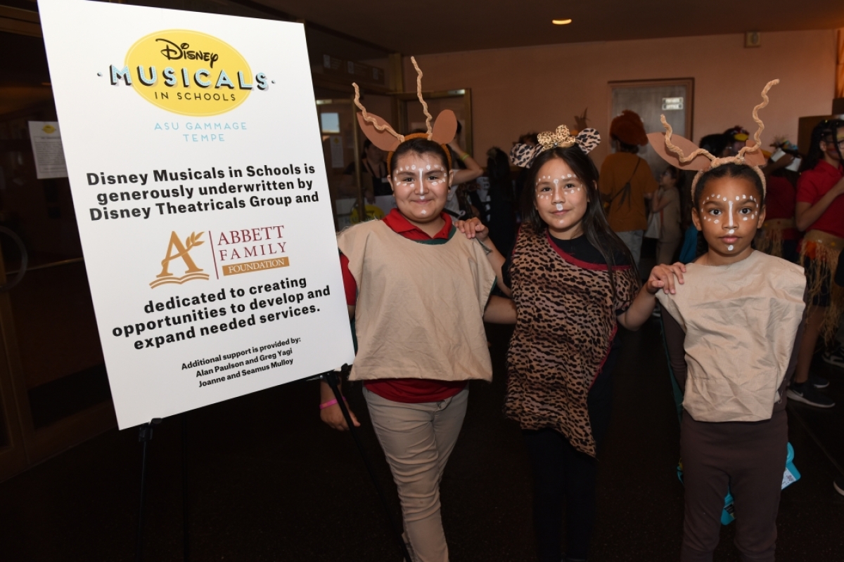 Three children in costume standing next to a Disney Musicals in Schools sign.