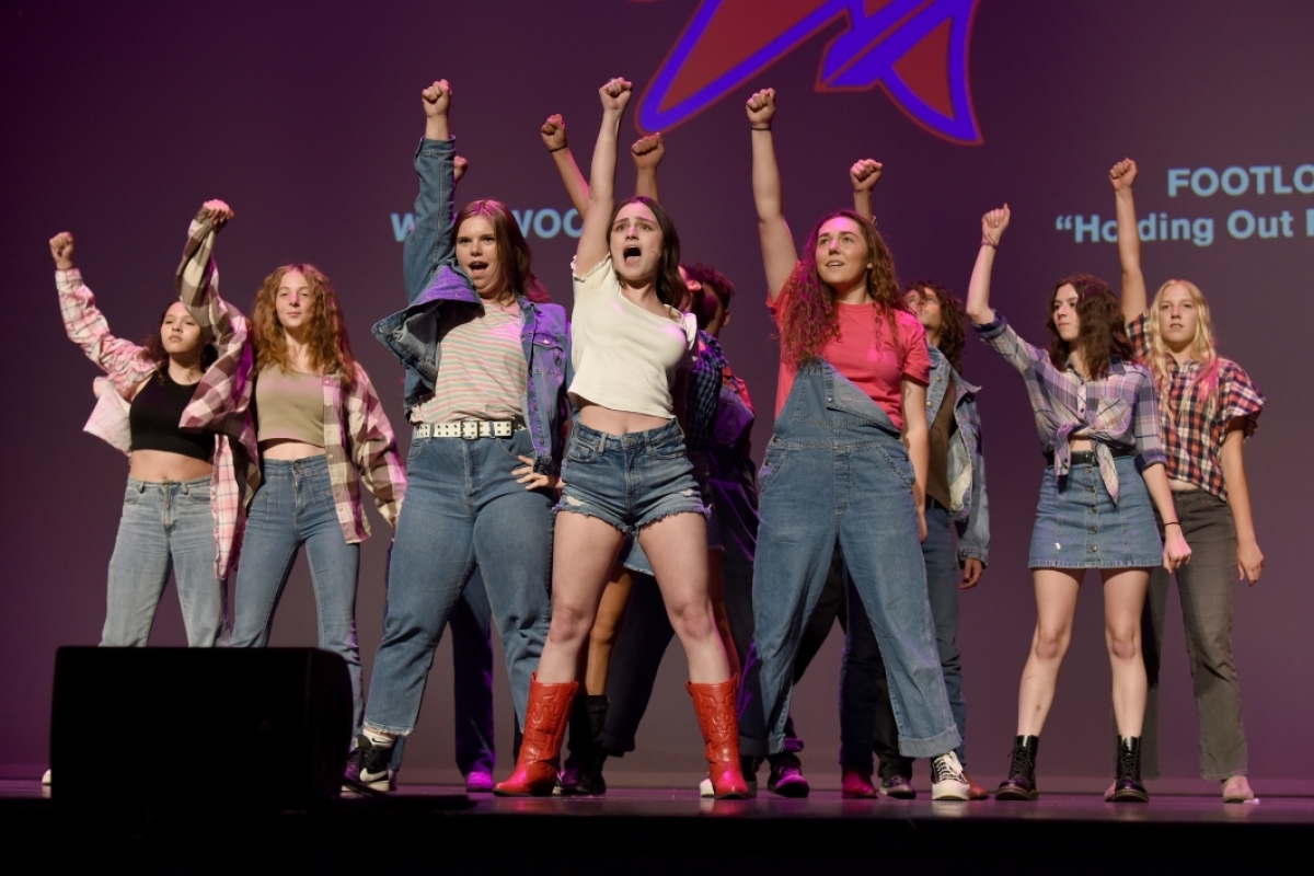 A group of performers stand together on stage with arms and fists raised.