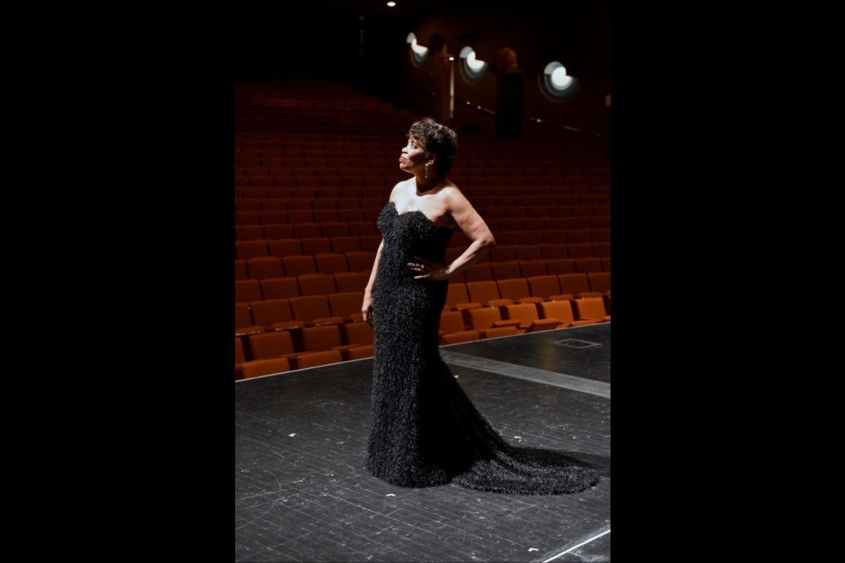 Woman in a black gown poses with her hand on her hip in front of an empty theater.