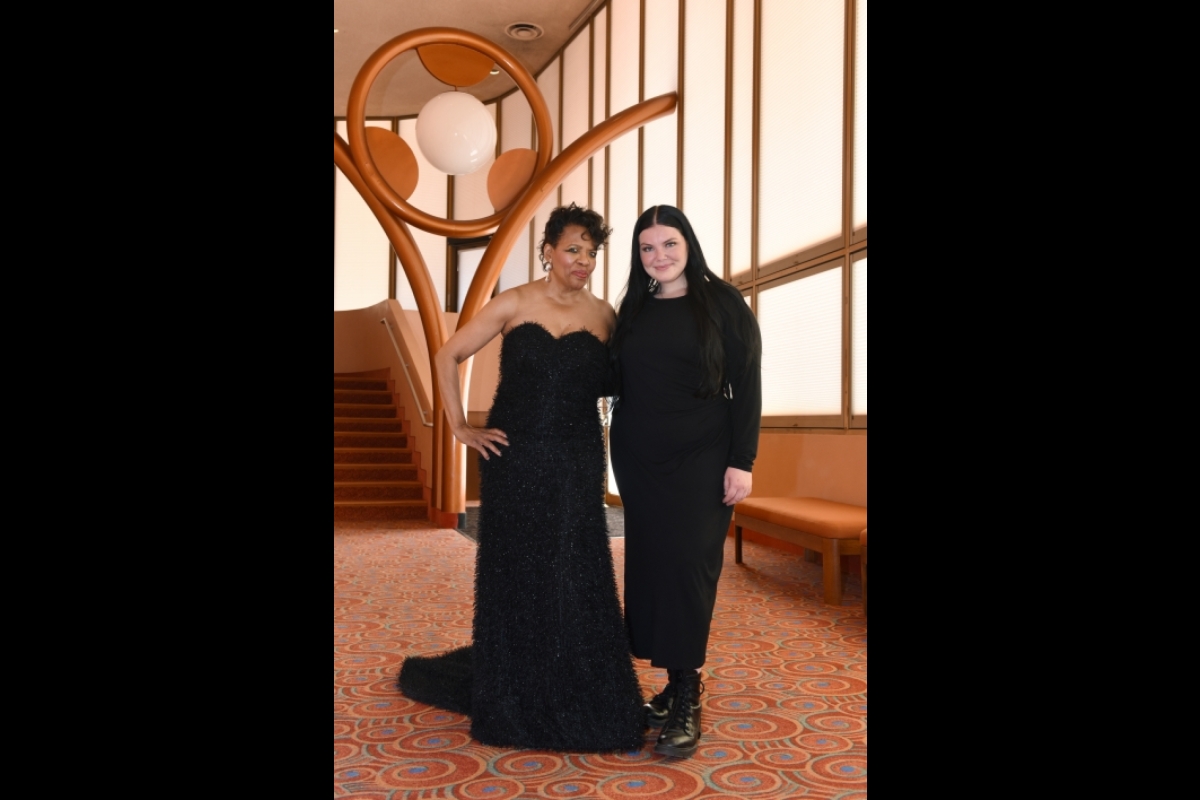Two women dressed in black pose for a photo together.