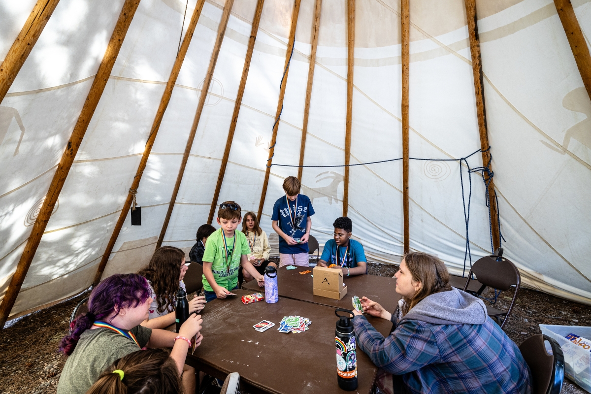 Kids play uno in a tent during camp