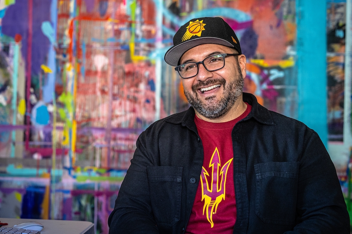 Miguel Godoy smiling in front of a colorful mural.
