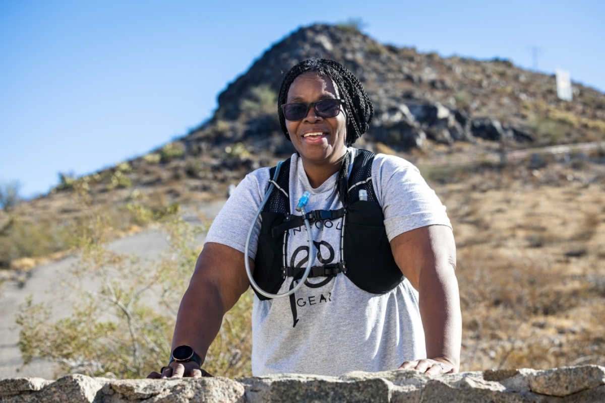 A hiker wearing a hydration vest smiles as she poses leaning on a low wall