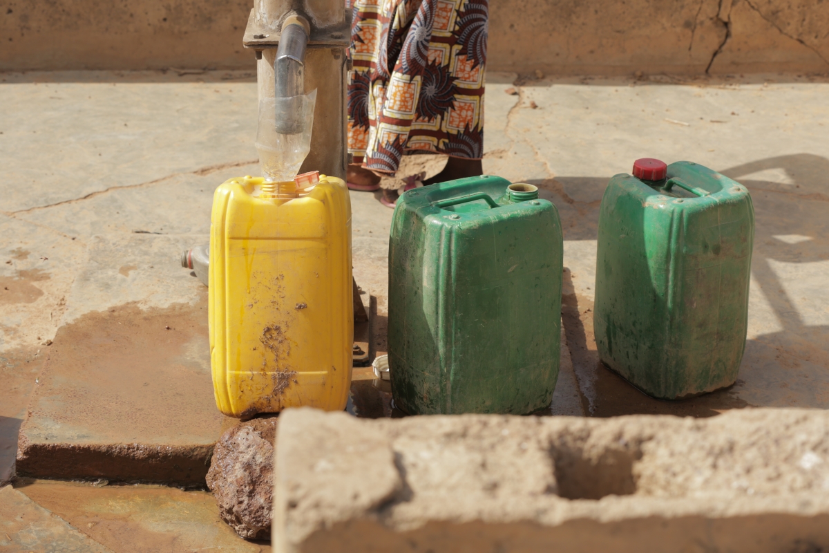 The feet of a Mossi woman are seen next to water cans.