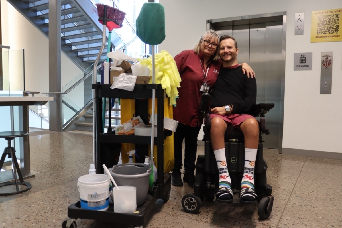 Man using a wheelchair posing with a woman standing next to a maintenance cart.