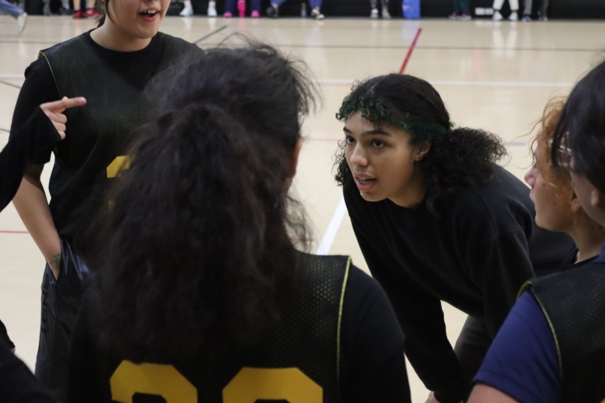Woman leaning in to talk to members of a basketball team in a huddle.