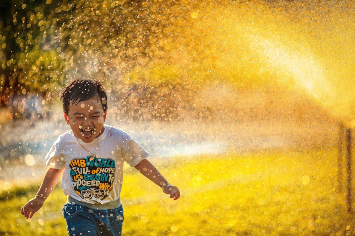 Child running through sprinklers outside.