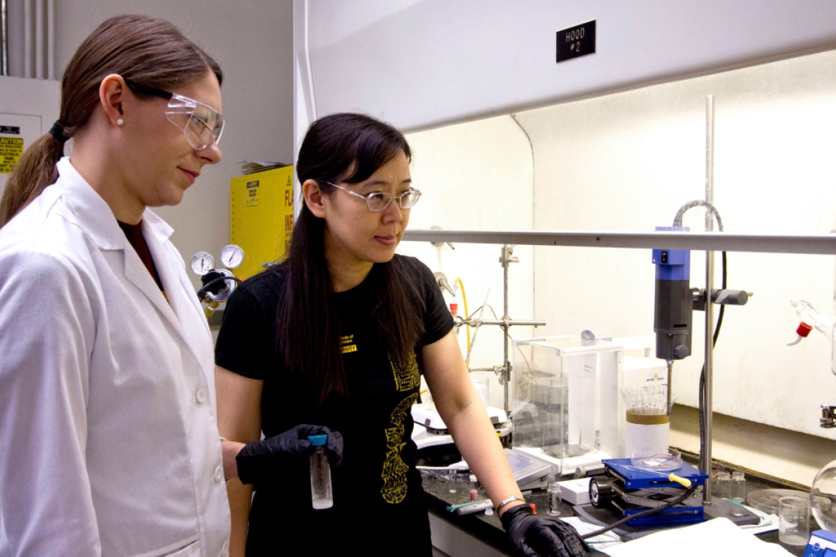 A doctoral student in a lab coat and her faculty advisor work together in a lab.