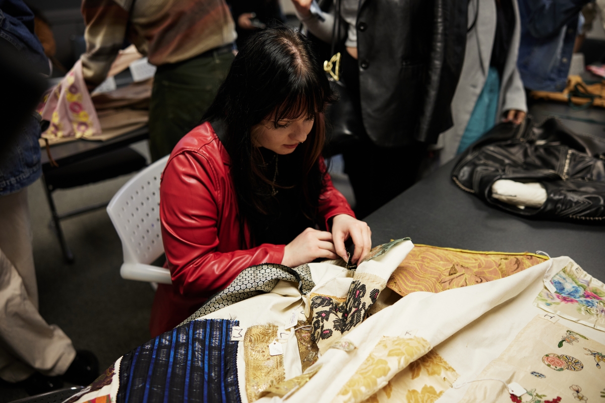 A student sits at a table looking at fabrics.