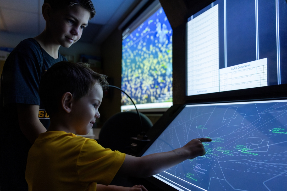 Two young boys pointing to a screen showing flight paths.
