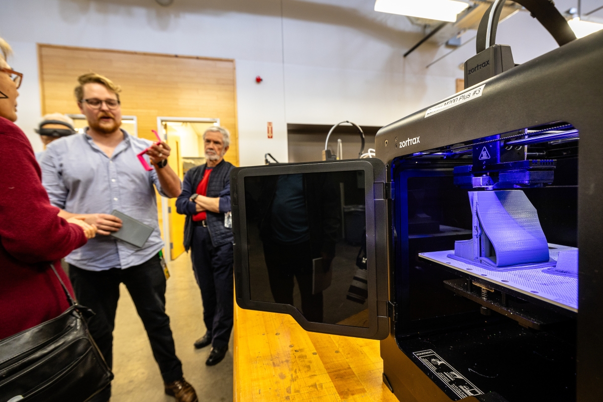 A man shows a 3D printer to a group of adults