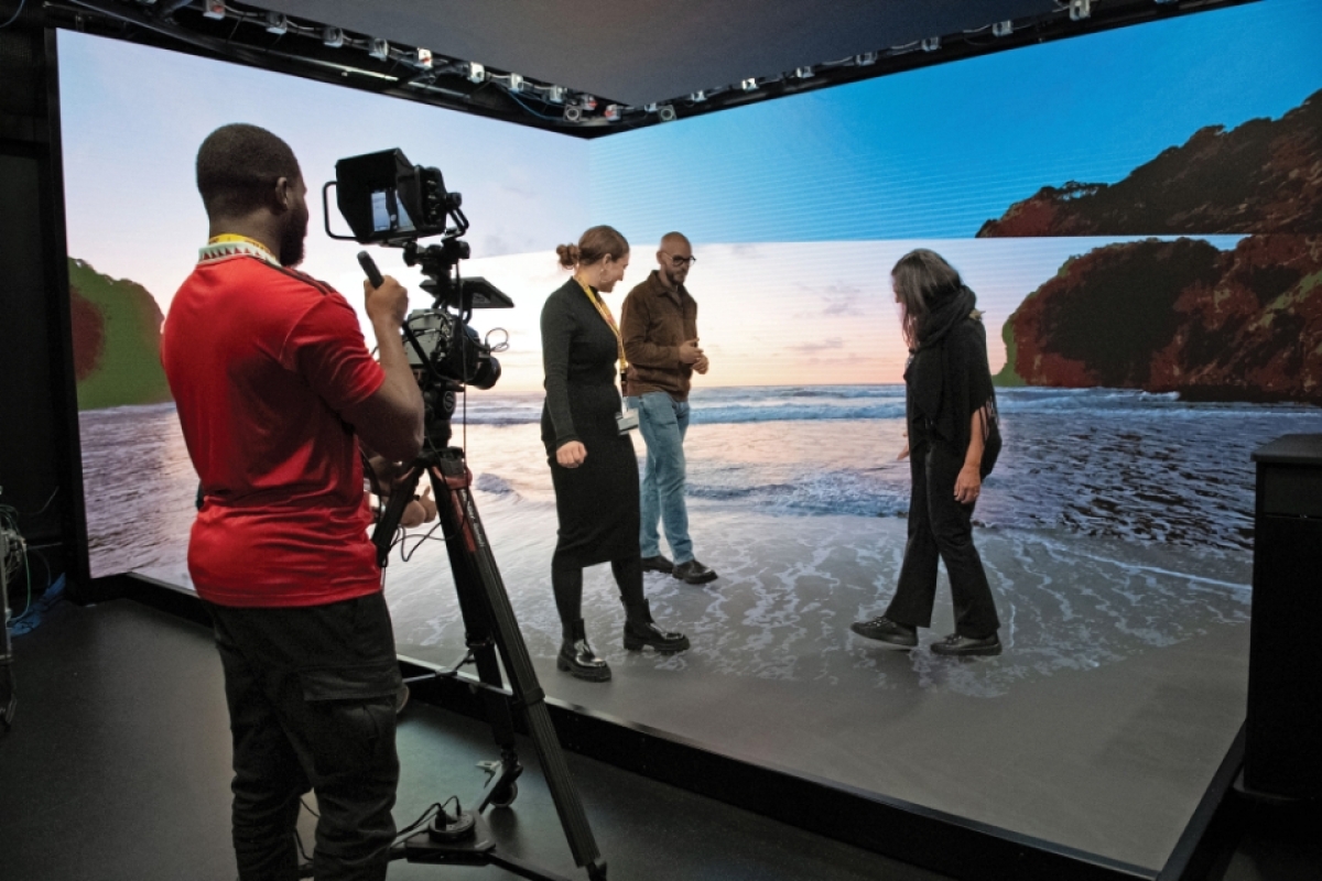 People on planar screen set that displays a 3-D rendering of the beach