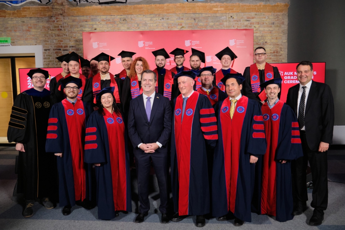 People wearing black graduation robes and red stoles pose with a man in a suit.