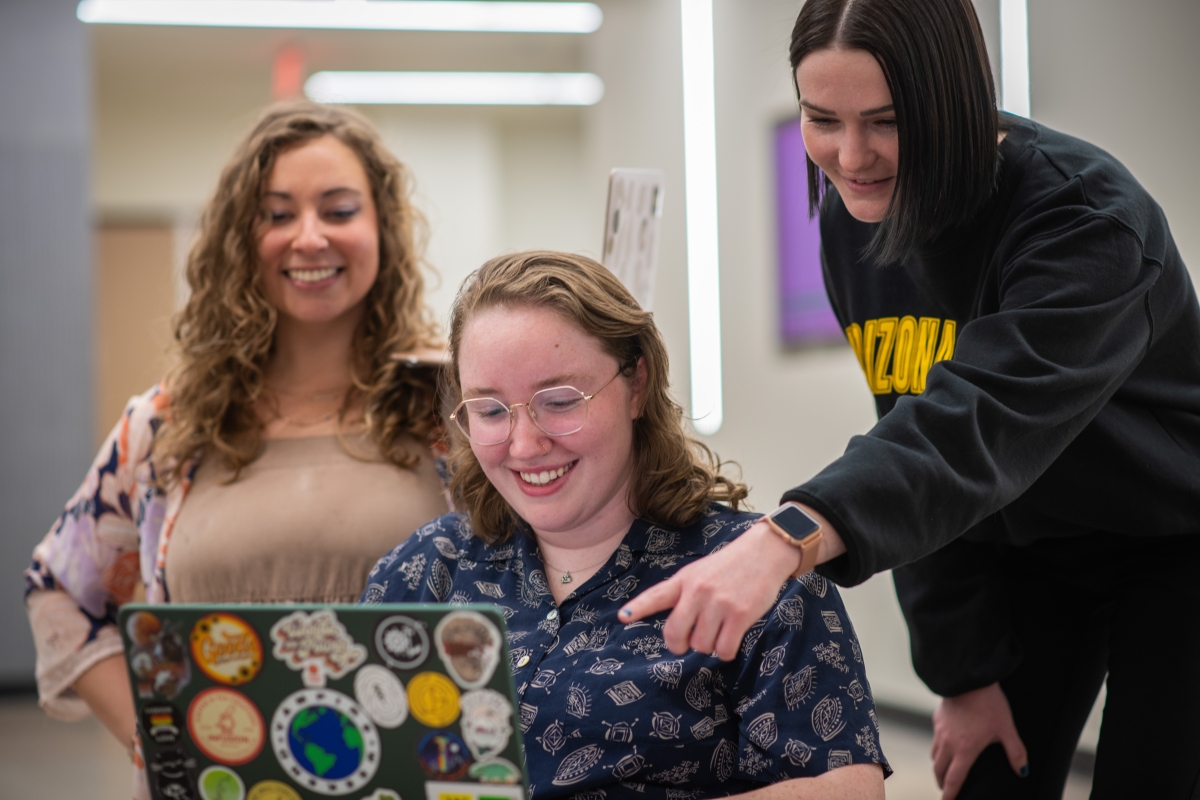 Three female graduate students gather around laptop during class