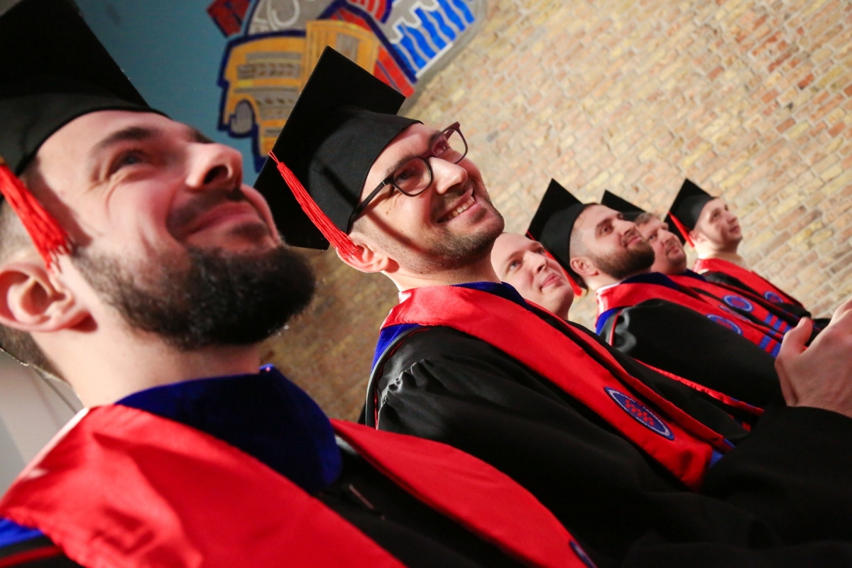 People wearing black graduation robes and red stoles smiling.