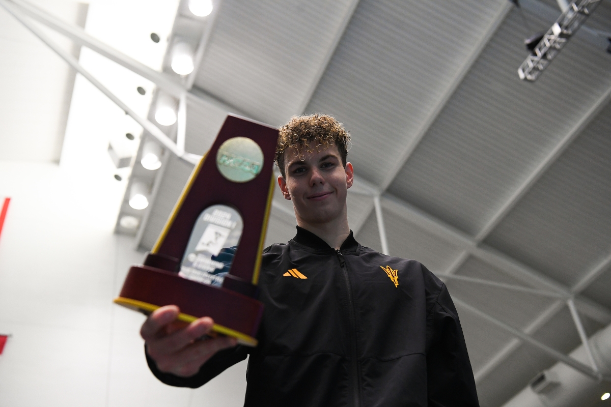 A swimmer smiles as he holds an NCAA trophy