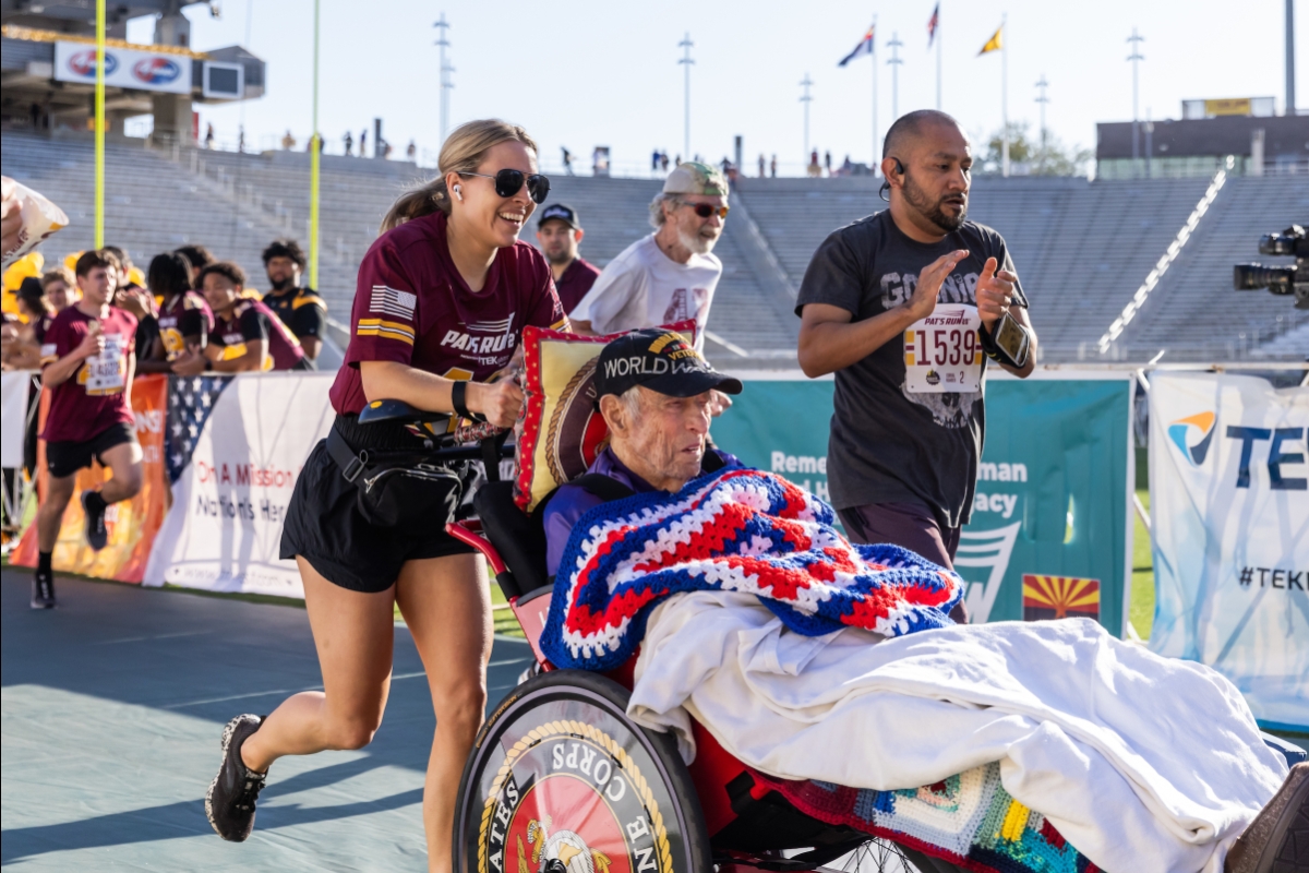 A woman pushing a man in a wheelchair across race finish line