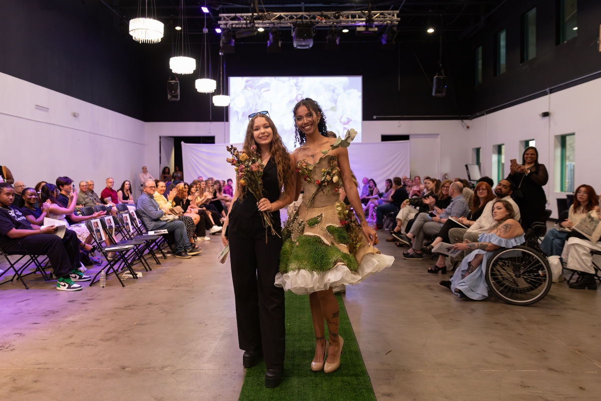 Designer and model in sustainable flower dress pose on runway