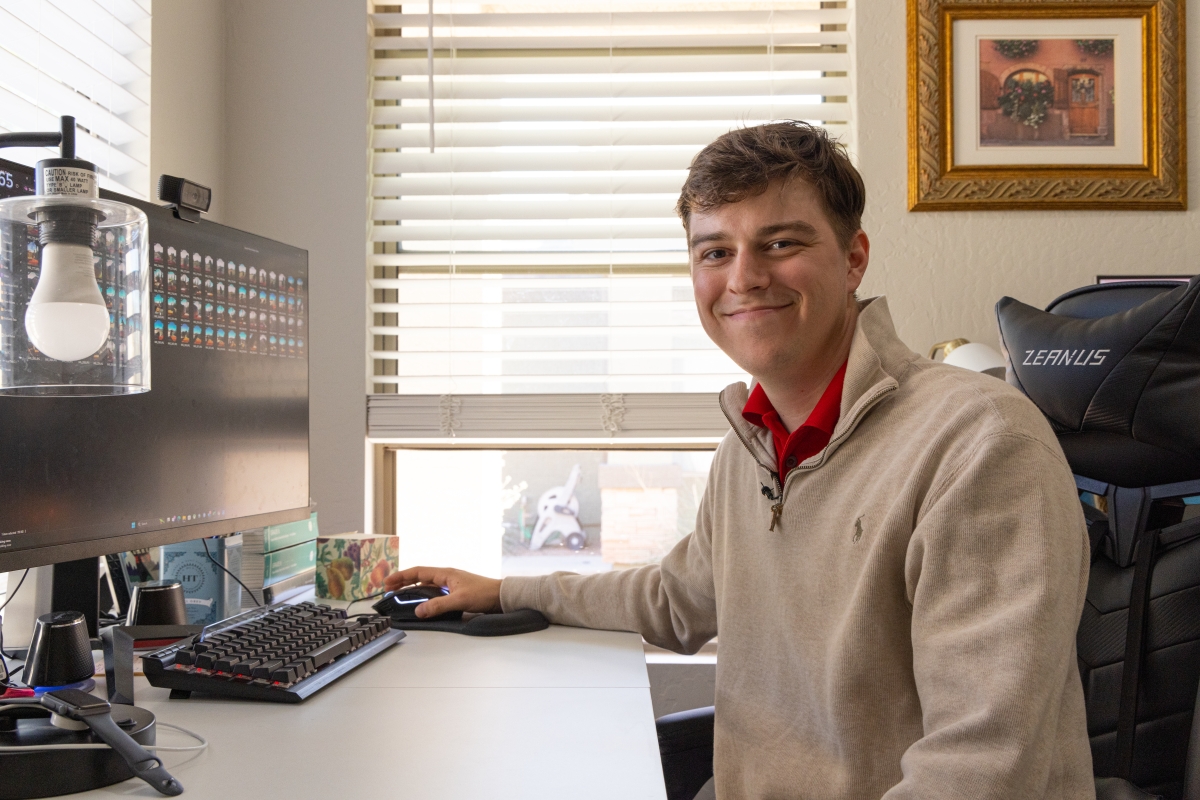 Photo of Carter Snee at his computer desk smiling into the camera.