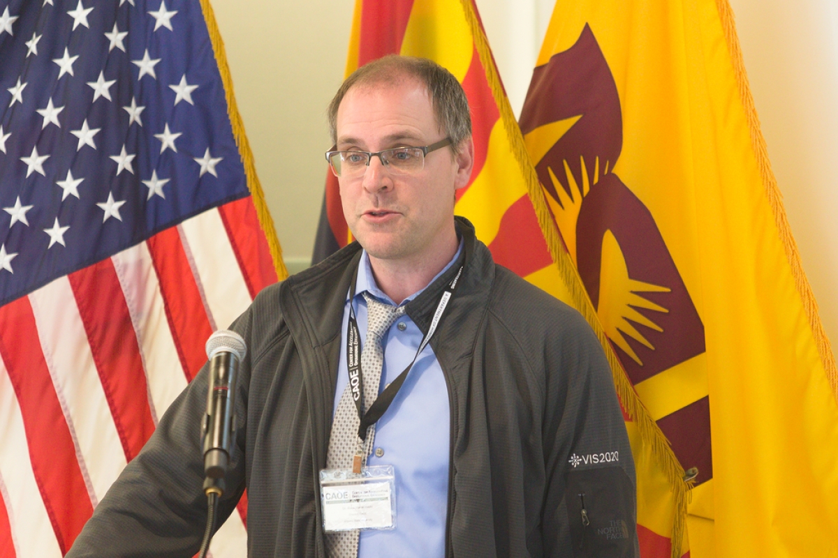 Ross Maciejewski speaks to an unseen audience with ASU, Arizona and American flags in the background.