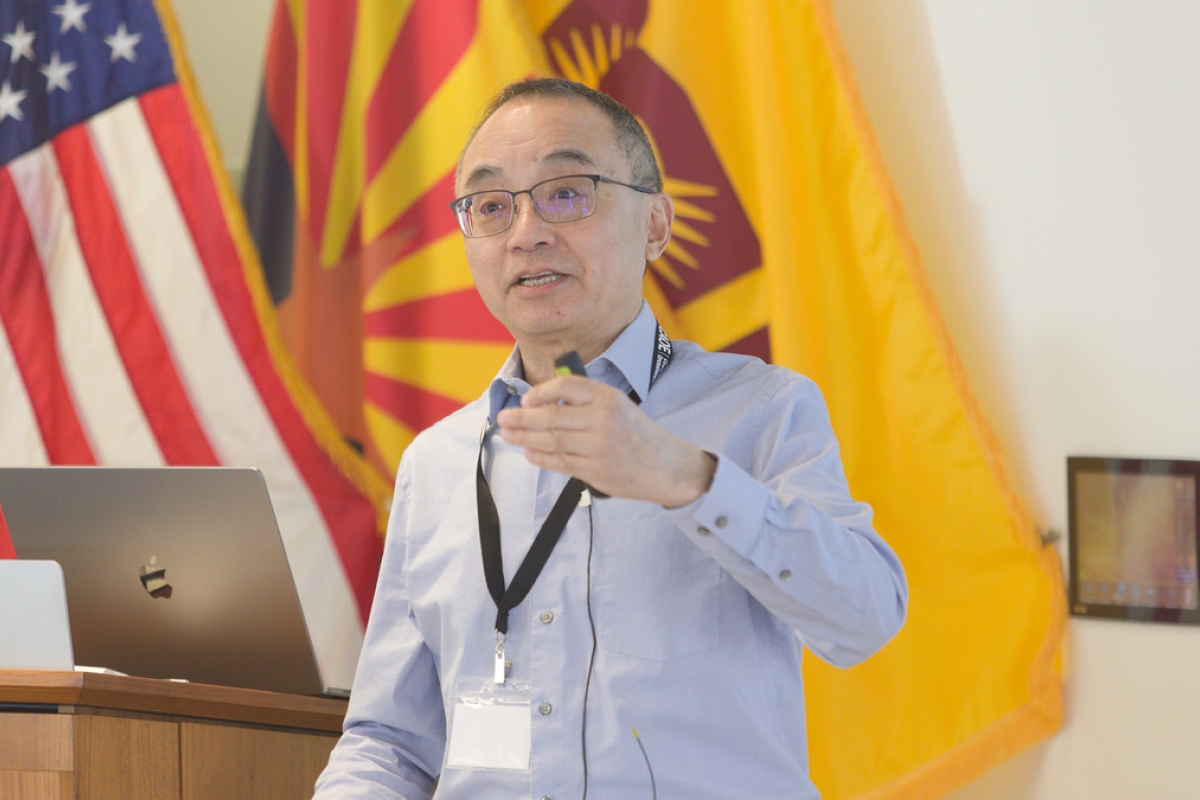 Huan Liu speaks to an unseen audience with ASU, Arizona and American flags in the background