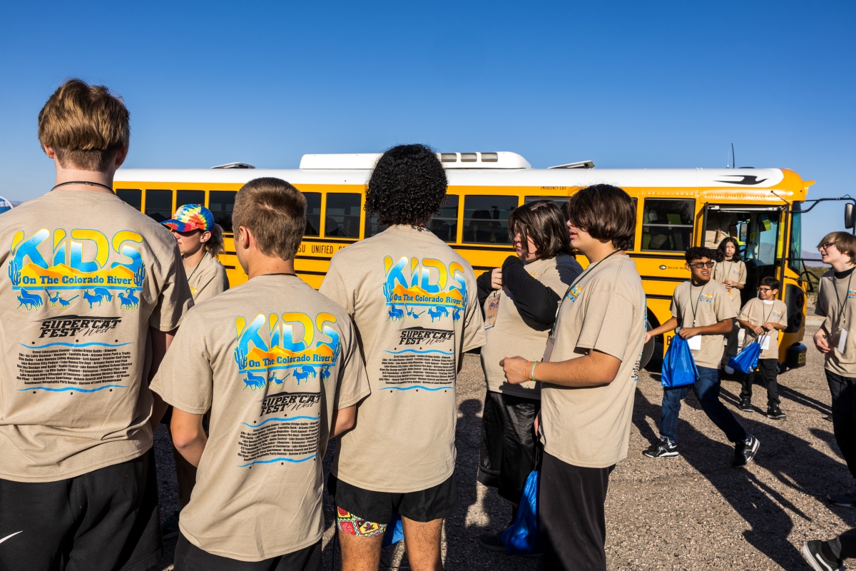 A group of kids wearing the same t-shirt stand in front of a bus